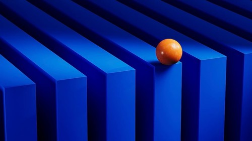 An orange sphere balances on blue geometric forms, creating a vibrant contrast against the