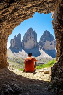 Hiker admiring the tre cime di lavaredo from inside a mountain Tre Cime Cave during a sunny summer