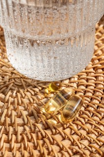 Close-up view of Omega 3 fish oil and vitamin D3 capsules on a woven rattan tray alongside a glass