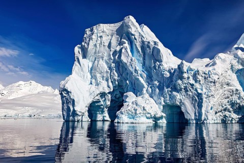 Imposing icebergs are reflected in the calm water under a clear blue sky, icebergs in the Southern