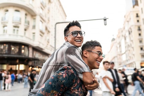 A cheerful latin gay couple enjoying a playful piggyback ride on a lively street in Madrid,