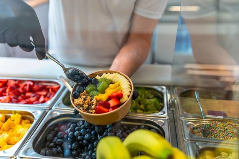 Person wearing gloves preparing a nutritious acai smoothie bowl, adding fresh blueberries, sliced
