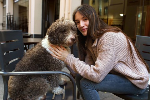 A young woman with long hair and a cozy sweater lovingly embraces her fluffy brown and white dog