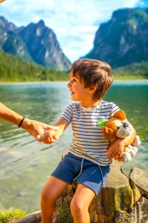 Smiling child holding a plush toy and his parent's hand while enjoying a summer day at lake