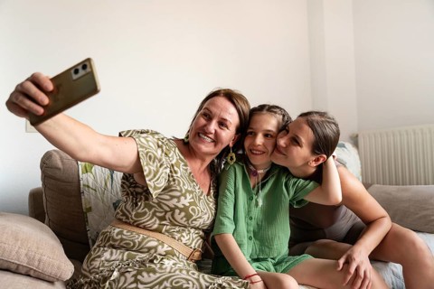 A joyful family is gathered on the couch, taking a selfie with a young girl who has a tracheostomy.