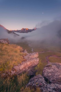 A breathtaking mountain landscape at dawn, with a rocky foreground, misty valley, winding stream,