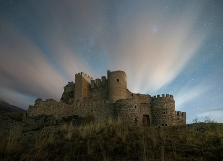 Night falls over the Manqueospese Castle in Avila, Spain, with star trails shimmering above its