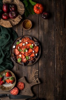 Anonymous people preparing a healthy tomato and strawberry salad on a wooden rustic table