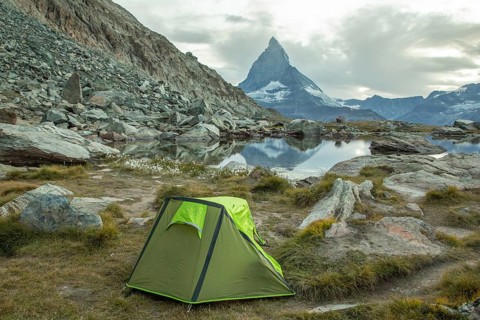 A vibrant green tent is set by a tranquil alpine lake, with the majestic Matterhorn towering in the