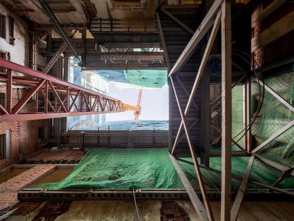 Looking up inside a building under construction, steel beams, scaffolding, and a towering crane