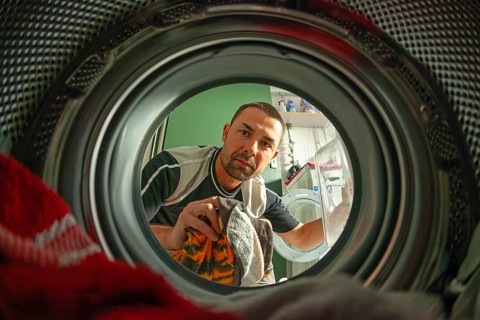 Man loads laundry, looking into washer from inside drum, home chore scene