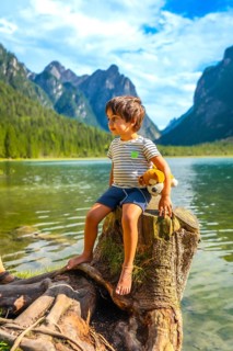 Young boy sitting on a tree stump by lake dobbiaco, holding his plush toy and admiring the