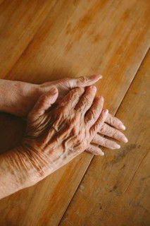 Close-up of elderly hands gently resting on a wooden table, capturing the texture and warmth of