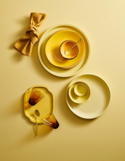 Top view of a stylish yellow ceramic crockery set, including plates, bowls, cups, and a golden