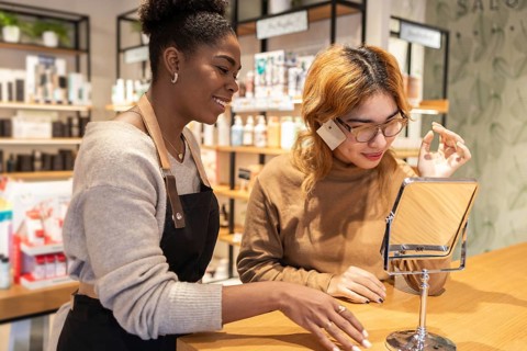 A employee in a cosmetics store help a customer with makeup. She is focused on providing excellent