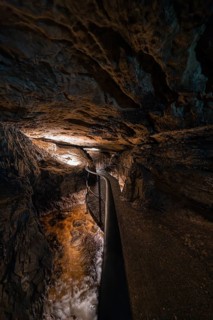 Narrow path in an illuminated cave with flowing water, gloomy adventure atmosphere, Beatus Caves,
