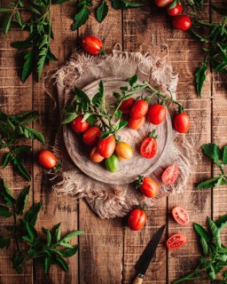 Fresh vine tomatoes are artistically arranged on a rustic wooden table, surrounded by green leaves,