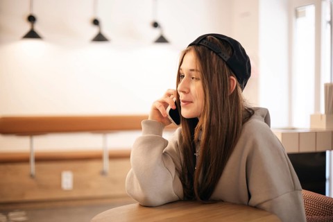 A teenage girl in a cozy coffee shop is engaged with her smartphone, wearing a casual hoodie and a