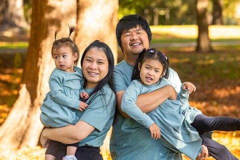 A joyful Asian family with parents and two young children, smiling and playing together in a sunny