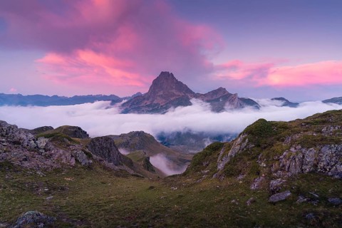 A breathtaking mountain peak surrounded by clouds at sunrise in the Pyrenees. The vibrant pink sky