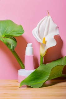 Eco-conscious cosmetic bottles styled with vibrant green leaves and a white flower against a soft