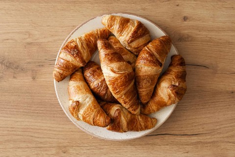 A top view of freshly baked homemade croissants arranged on a white plate, placed on a wooden