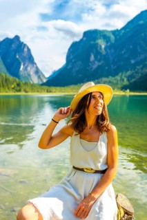 Young woman wearing a straw hat relaxing at lake dobbiaco with the dolomites in the background,