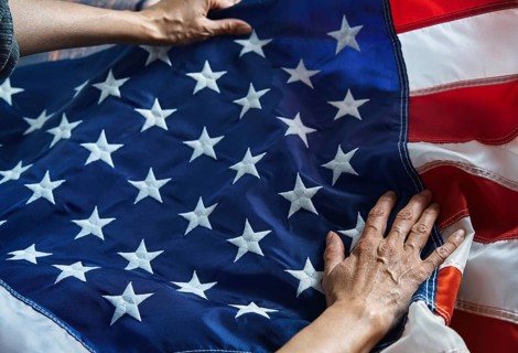 Hands gently hold the American flag, with its iconic stars and stripes. This image symbolizes