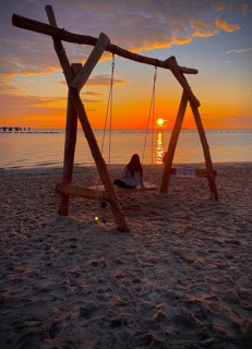 Young girl sitting on a swing on the beach watching sunrise on the island of Rügen,