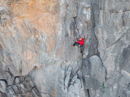 A climber skillfully ascends a rugged cliff face, showcasing traditional climbing techniques amidst