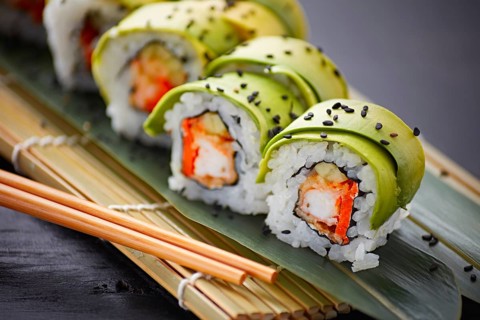 Delectable sushi rolls, elegantly wrapped in slices of avocado, served on a traditional bamboo mat.