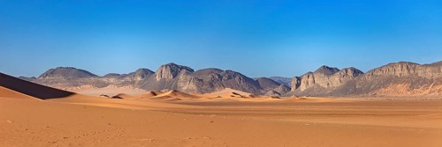 Gentle sand dunes with mountains in the background and a bright blue sky, The landscape of the