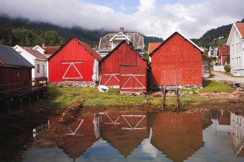Charming red wooden huts reflect in the calm water of a Norwegian fjord village Surrounded by lush