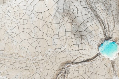 Aerial view of cracked earth with intricate lines and a vibrant blue water body in the corner. This