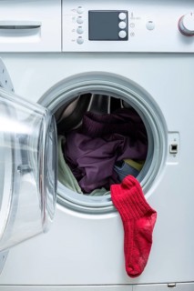 A bright red sock hangs from the door of an open front-load washing machine filled with laundry,