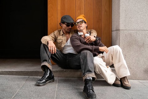 A Colombian gay couple sits on a city street, embracing while enjoying a casual moment. Wearing