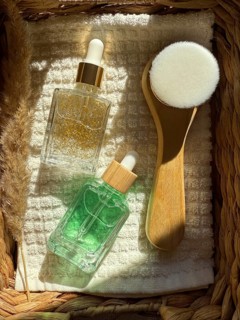A top down view of two serum cosmetic bottles and a facial brush arranged on a textured surface in