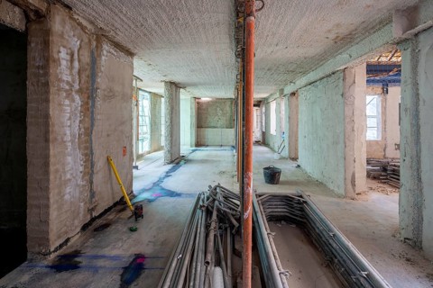 Unfinished building interior showcases raw concrete walls, scattered tools, and construction