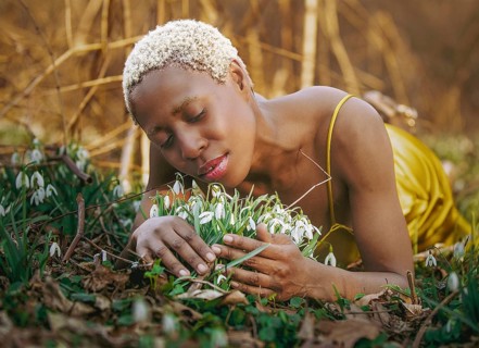 A woman in a golden dress lies peacefully among blossoming snowdrops, enjoying nature tranquility