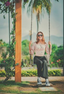 Portrait of a smiling girl sitting on a swing in a nature park. Happy young woman sitting on a
