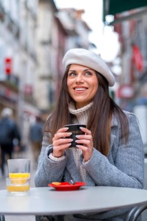 Vertical photo of a chic woman drinking hot coffee in an outdoors cafeteria during a cold day