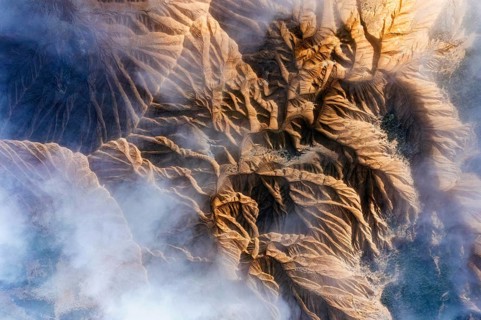 An aerial view showcases rocky mountain formations with deep ridges and valleys Wisps of mist
