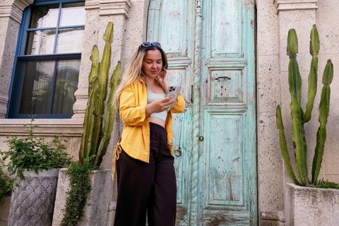 A female tourist stands in front of an ornate wooden door, intently using her smartphone to