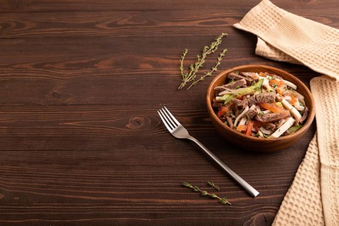 Meat salad with beef and vegetables in wooden bowl on brown wooden background and linen textile.