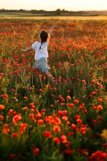 Back view of unrecognizable girl joyfully running in a lush field filled with blooming Papaver