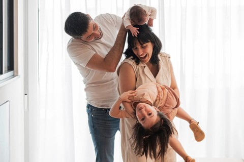 Happy young family shares joyful moments at home. The father holds a newborn while the mother