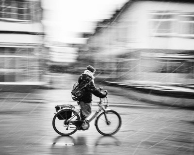 A person on a bicycle rides through a city in bad weather and sleet, rainy day black and white