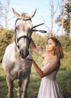 A young woman in a white dress gently touches a white horse face amidst a tranquil countryside