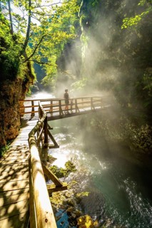 Sunbeams illuminating mist rising from radovna river in vintgar gorge near bled, with tourist