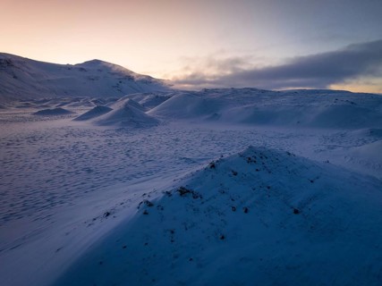 A serene winter twilight spreads over snow-draped hills in Iceland, capturing the tranquil beauty